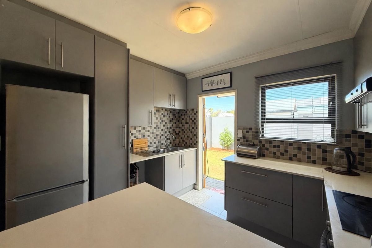 Modern kitchen featuring grey cabinetry, mosaic tile backsplash, built-in hob, extractor fan, and direct access to the rear garden area.
