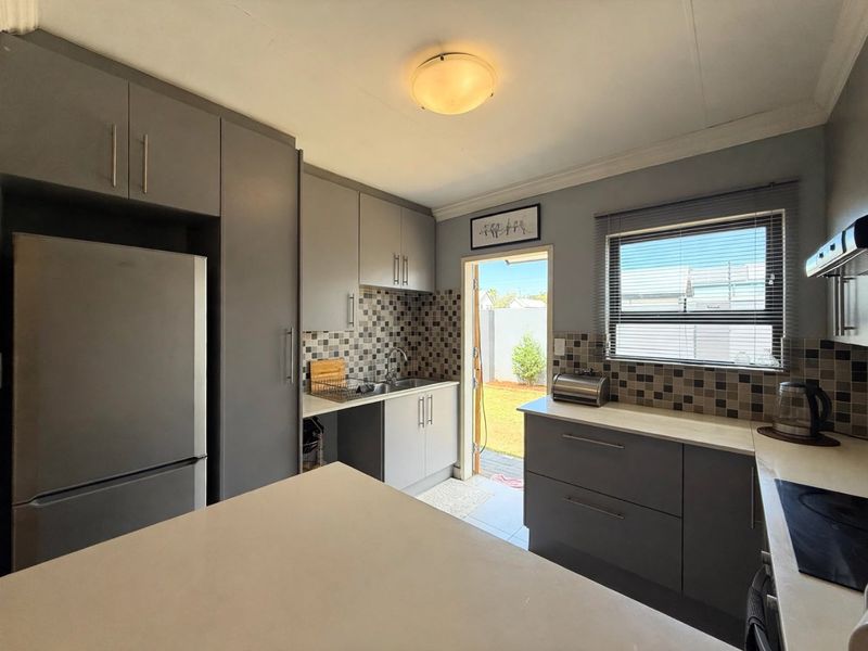 Modern kitchen featuring grey cabinetry, mosaic tile backsplash, built-in hob, extractor fan, and direct access to the rear garden area.
