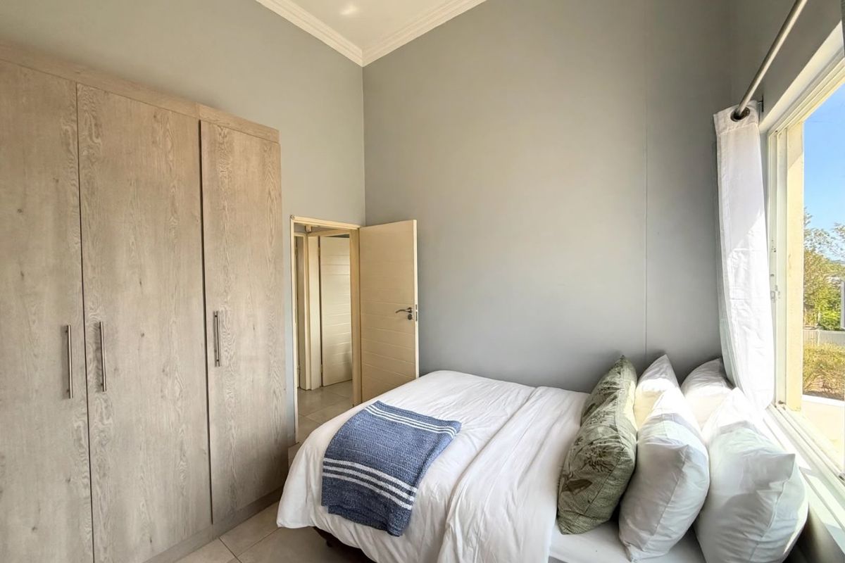 A well-maintained bedroom featuring neutral grey walls, tiled flooring, and a large built-in wardrobe with wood-grain finish.