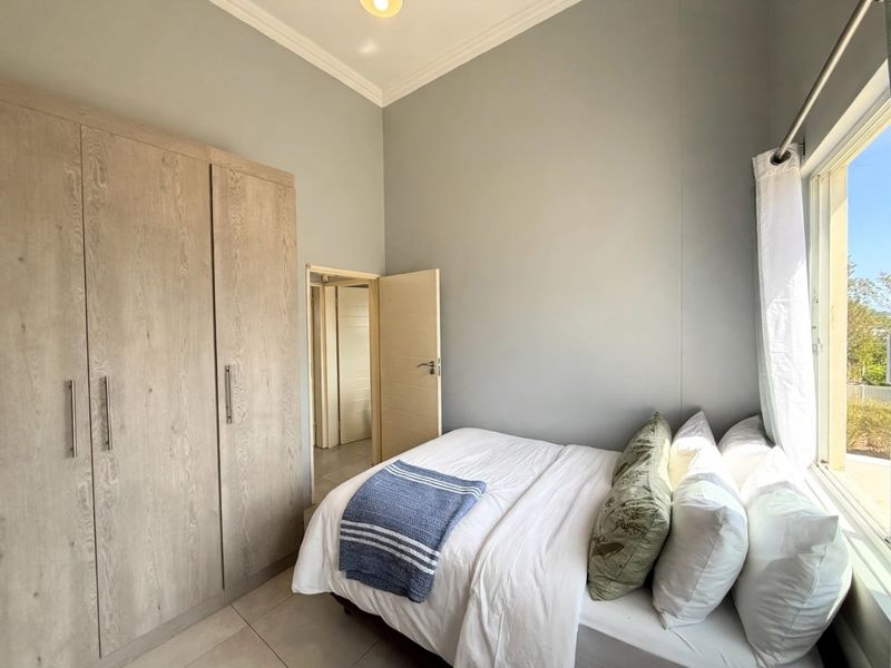 A well-maintained bedroom featuring neutral grey walls, tiled flooring, and a large built-in wardrobe with wood-grain finish.
