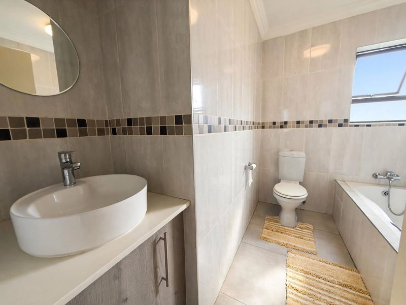 A clean, modern bathroom featuring a vessel sink vanity, a built-in bathtub, and neutral wall tiling with a decorative mosaic accent border.