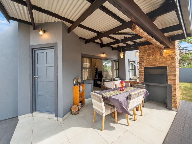 A covered outdoor patio featuring a built-in brick braai, exposed timber beams, and tiled flooring, providing a functional space for outdoor dining and entertainment.