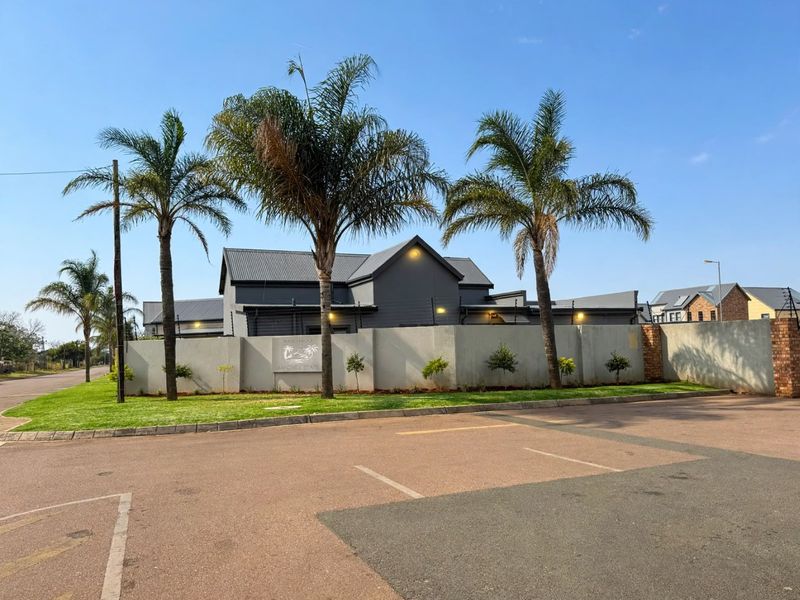 Front exterior view of the property featuring a secure perimeter wall with electric fencing, metal roofing, and well-maintained landscaped grounds.