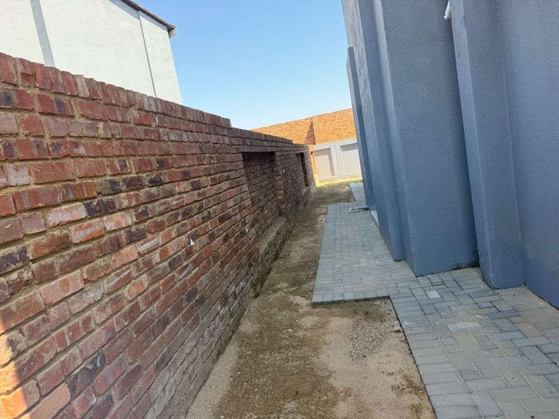 A side passage featuring a brick boundary wall and a paved walkway alongside the main structure of the house.