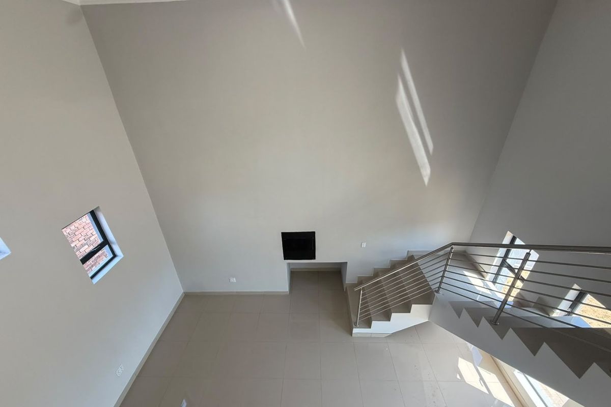 Spacious double-volume living area featuring tiled flooring, a built-in fireplace, and a modern staircase with a stainless steel balustrade.