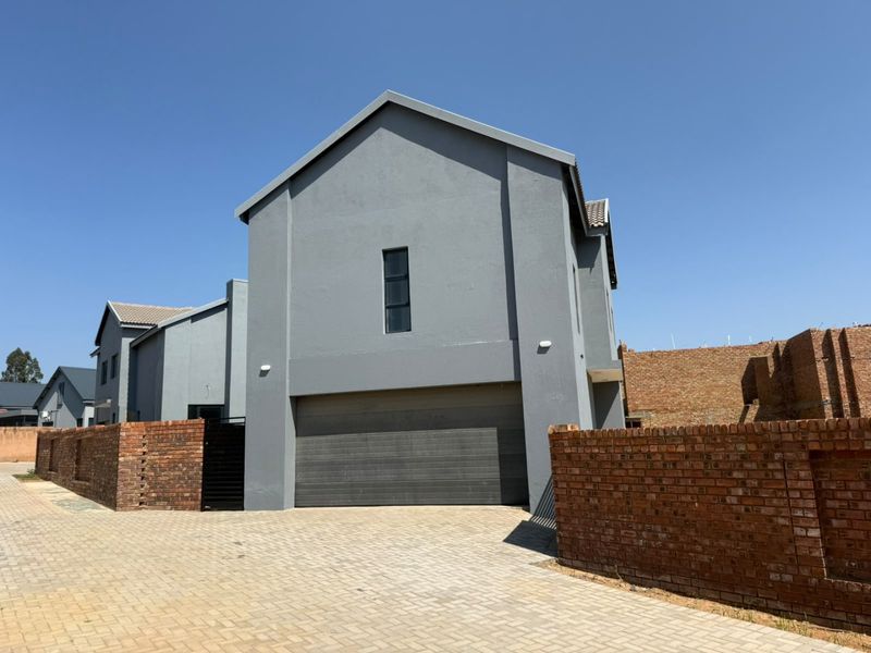 Front elevation of a modern double-storey house featuring a paved driveway, double garage, and brick boundary walls.