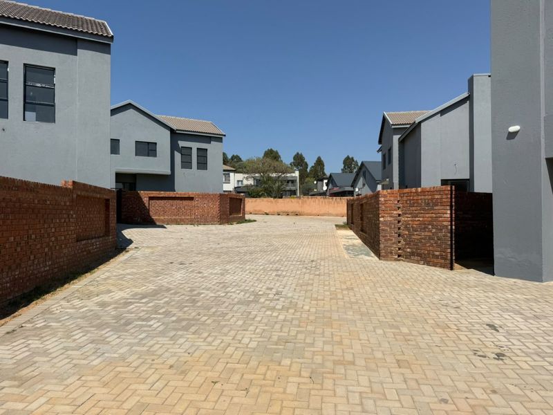 A view of the paved driveway and entrance area between modern grey residential units with brick boundary walls.