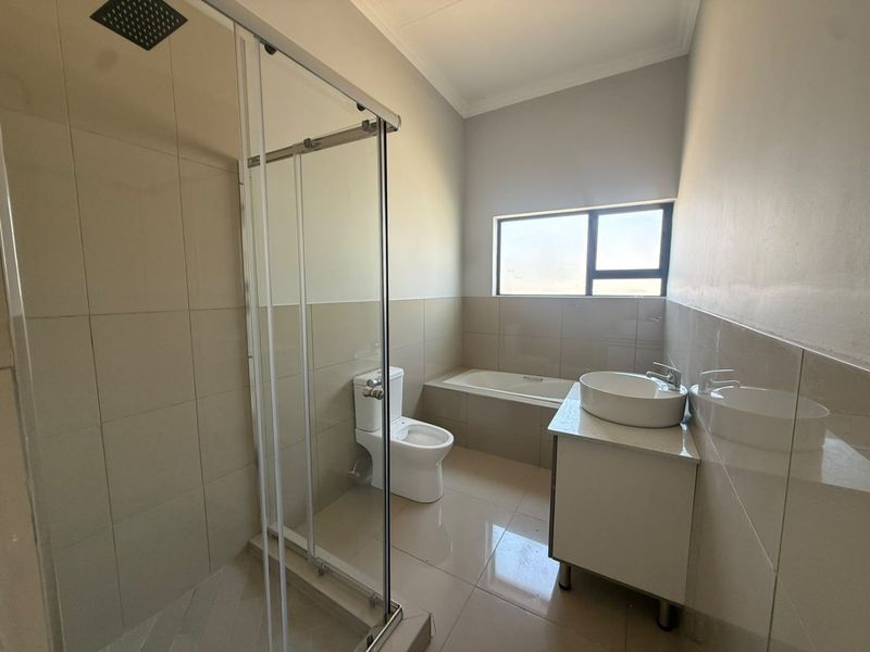 Modern bathroom featuring a glass-enclosed shower, built-in bathtub, vessel sink vanity, and neutral wall and floor tiling.