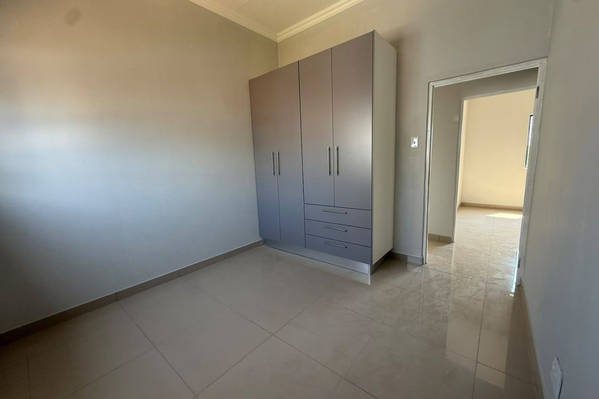 A clean, empty bedroom featuring neutral tiled flooring and a modern built-in wardrobe with integrated drawers.