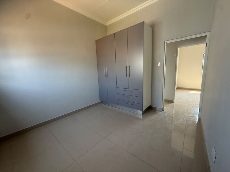 A clean, empty bedroom featuring neutral tiled flooring and a modern built-in wardrobe with integrated drawers.