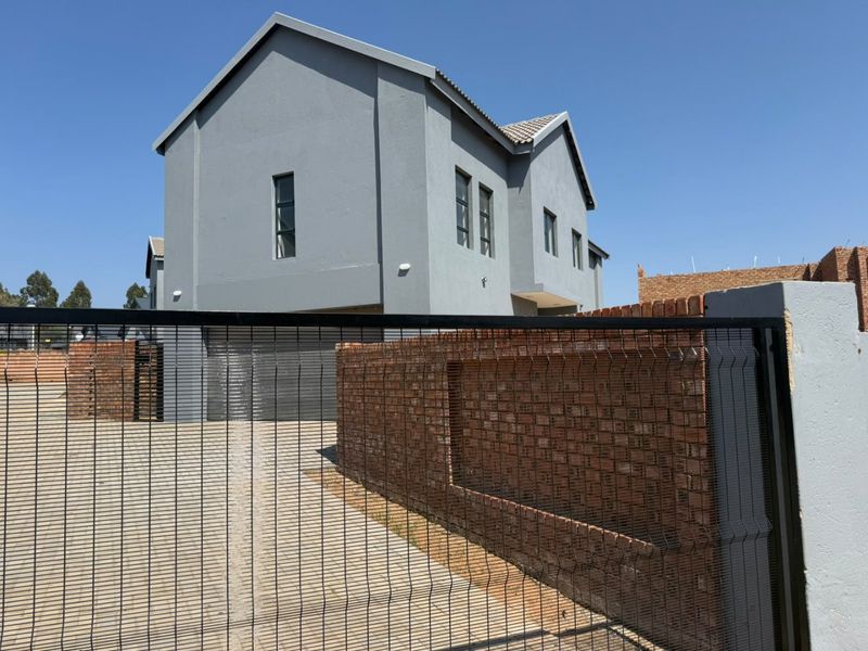 Front view of a modern double-story house featuring a paved driveway, double garage, and brick boundary wall with security fencing.