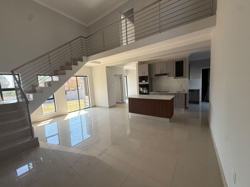 Spacious open-plan living area featuring a modern kitchen with island, sleek tiled floors, and a striking staircase with stainless steel balustrades.