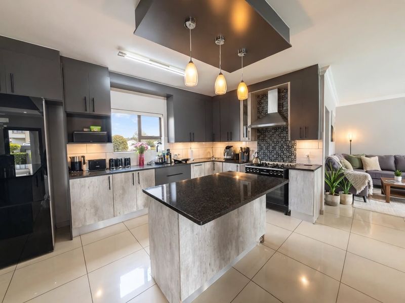 Modern open-plan kitchen featuring a central island, granite countertops, gas stove, and stylish pendant lighting, seamlessly flowing into the adjacent living area.