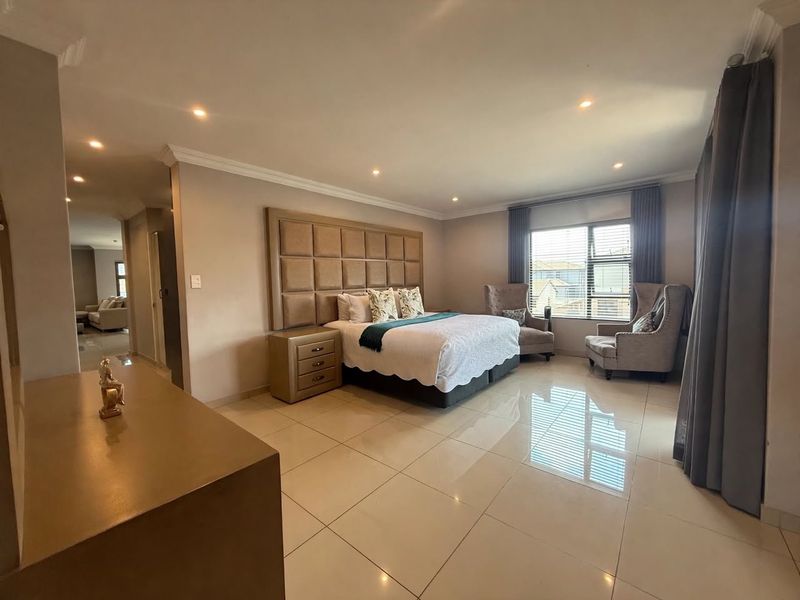 Spacious bedroom featuring polished tiled flooring, recessed downlighting, and a large integrated upholstered headboard, offering a clean and well-maintained living space.