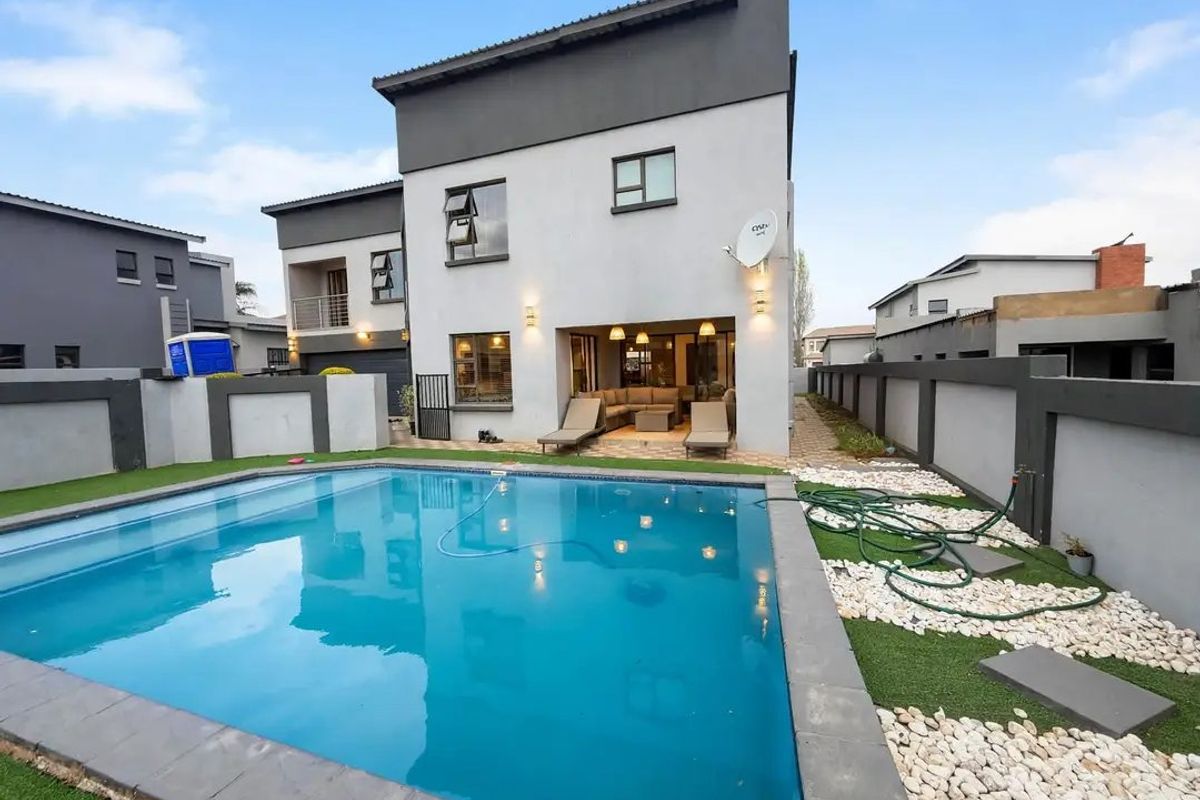 Rear view of a modern double-story house featuring a swimming pool, paved patio area, and enclosed garden with boundary walls.