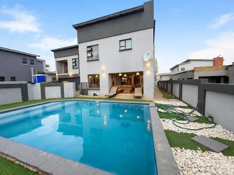 Rear view of a modern double-story house featuring a swimming pool, paved patio area, and enclosed garden with boundary walls.