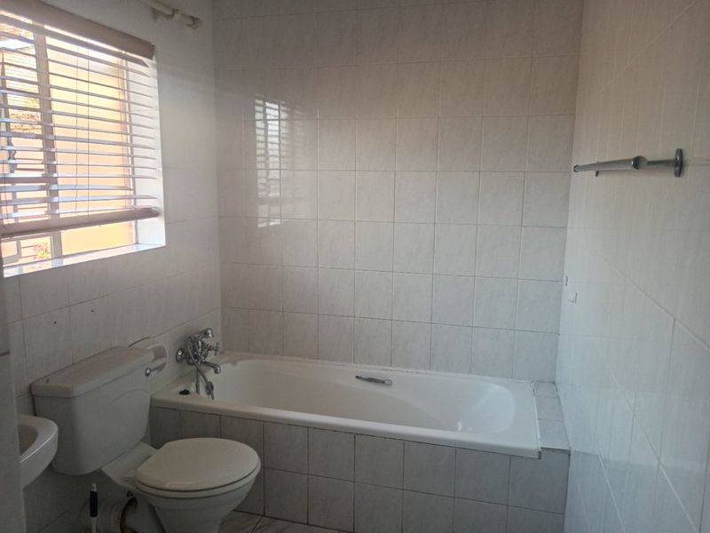 A functional bathroom featuring a built-in bathtub, toilet, and full-height wall tiling, offering a clean canvas for potential modern updates.