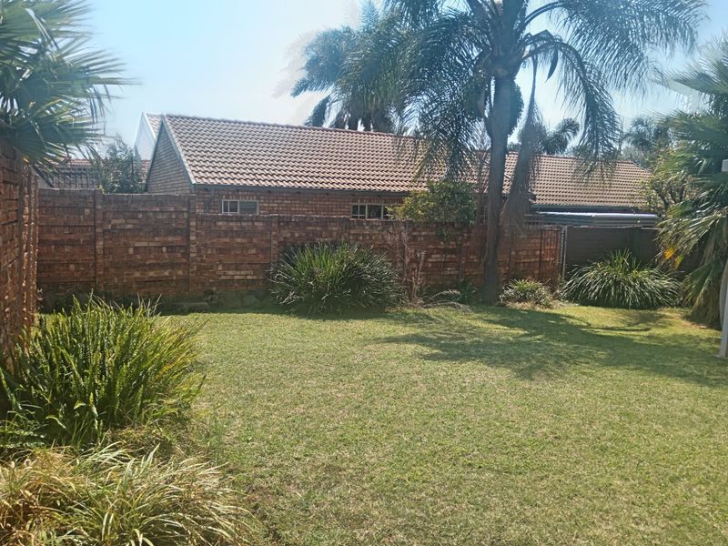 A private rear garden featuring a well-maintained lawn, mature palm trees, and a secure brick boundary wall.