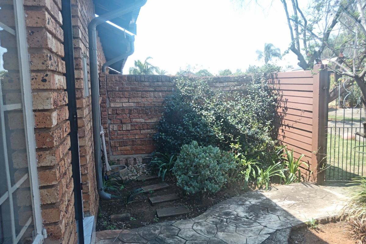 A rear exterior view of the townhouse featuring a face brick wall, paved walkway, and timber slat fencing with established garden landscaping.