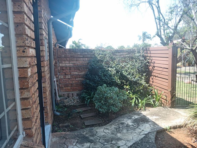 A rear exterior view of the townhouse featuring a face brick wall, paved walkway, and timber slat fencing with established garden landscaping.