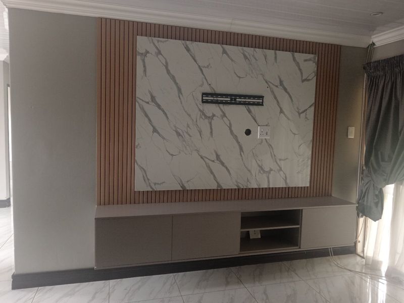 Modern living room featuring a custom built-in media console, marble-look feature wall with timber slat accents, and polished porcelain floor tiles.