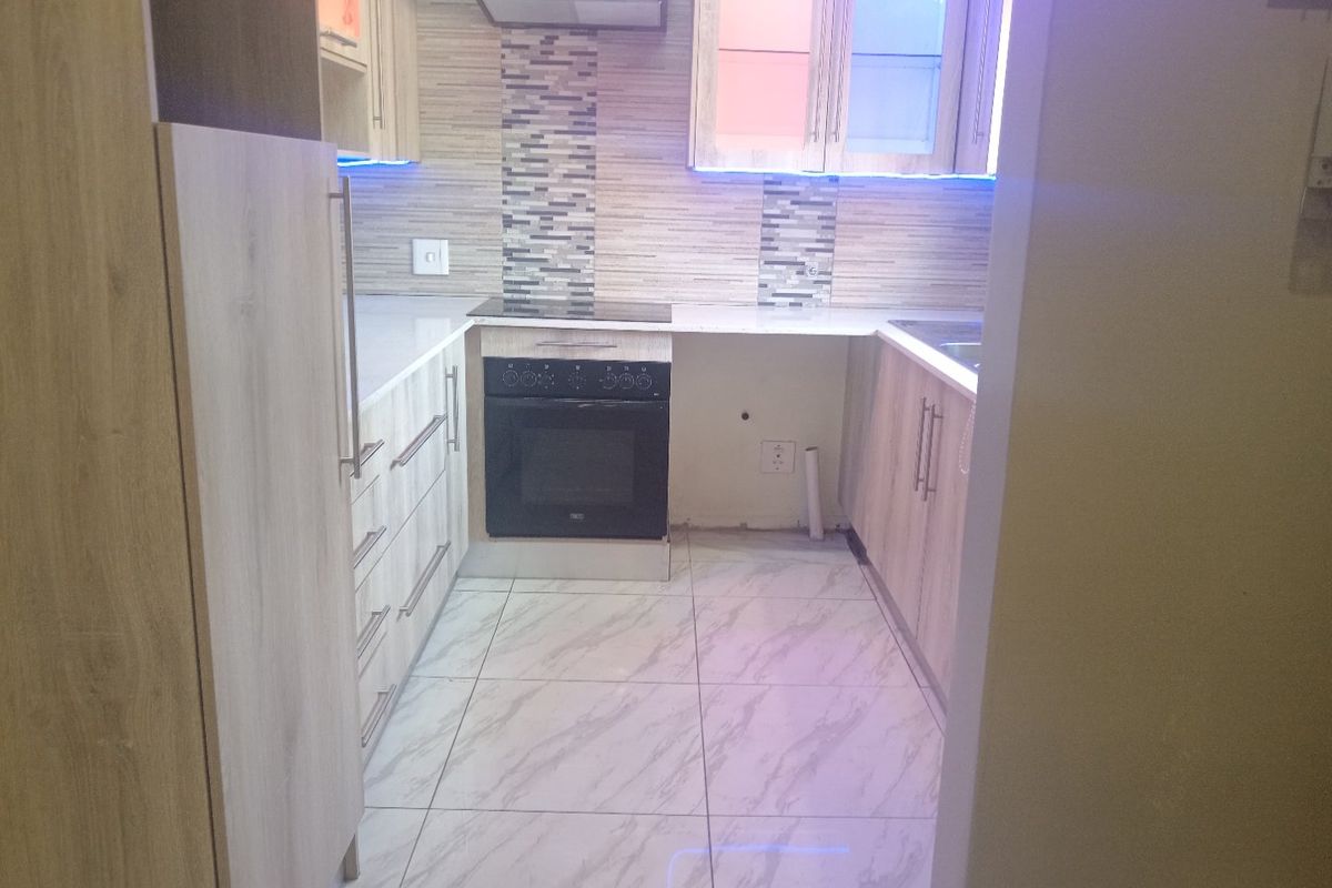A modern kitchen featuring light wood-finish cabinetry, mosaic tile backsplash, built-in oven and hob, and marble-look tiled flooring.