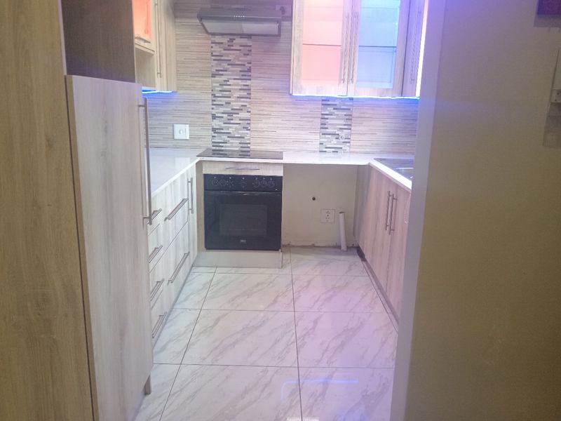 A modern kitchen featuring light wood-finish cabinetry, mosaic tile backsplash, built-in oven and hob, and marble-look tiled flooring.