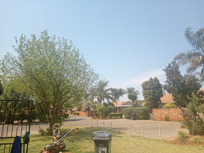 A view of the rear exterior area featuring a landscaped garden, paved parking spaces, and brick boundary walls within the townhouse complex.