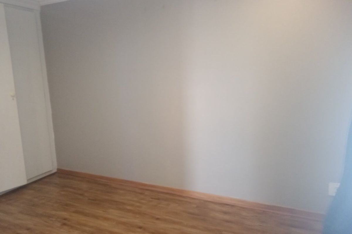 A clean, empty bedroom featuring laminate flooring, a built-in cupboard, and neutral wall finishes, providing a blank canvas for personalization.