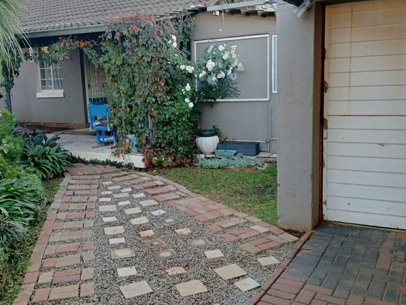 Front exterior view featuring a brick paved walkway leading to the entrance, a garage door, and a shaded outdoor area.