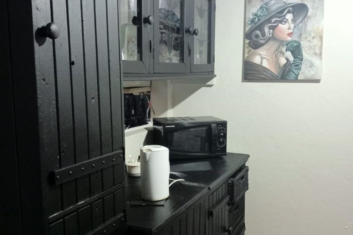 A small kitchen area featuring dark painted built-in cabinetry and laminate flooring, requiring some maintenance to the cabinetry and electrical finishes.