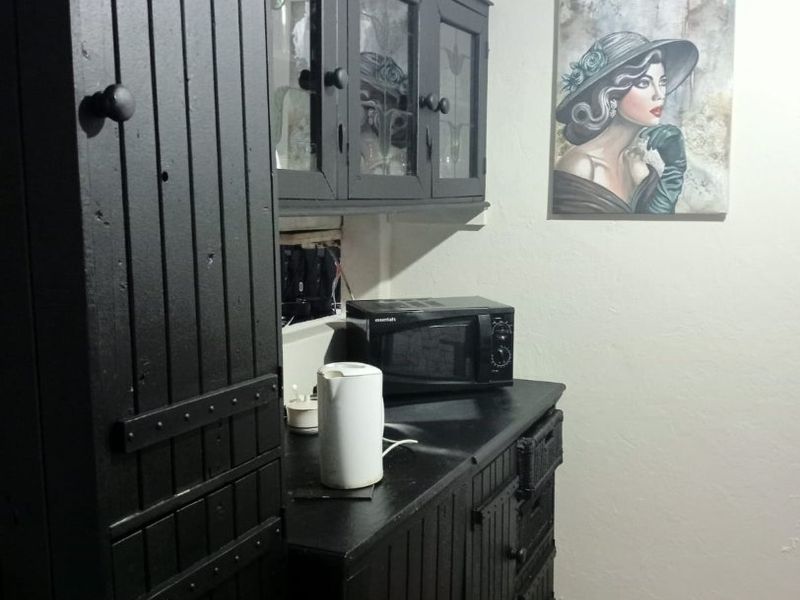 A small kitchen area featuring dark painted built-in cabinetry and laminate flooring, requiring some maintenance to the cabinetry and electrical finishes.