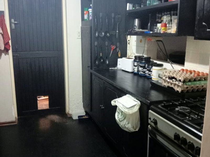 A compact kitchen featuring dark cabinetry, a gas stove, and a stable door with a pet flap, showing signs of wear on walls and flooring.