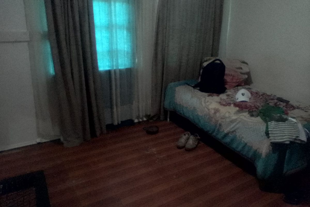 A bedroom featuring laminate flooring and a window with curtains, providing a functional space for rest.