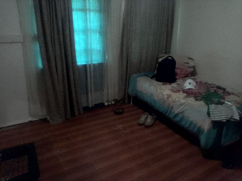 A bedroom featuring laminate flooring and a window with curtains, providing a functional space for rest.