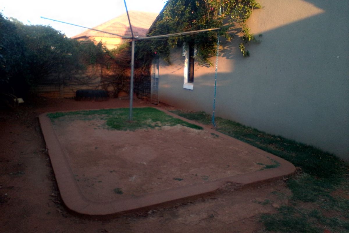 A rear garden area featuring a rotary clothesline, concrete garden edging, and an exterior wall with a window.