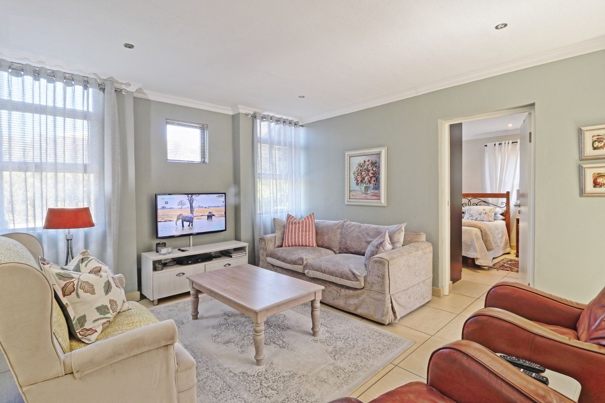 A comfortable living room featuring tiled flooring, recessed downlighting, and neutral wall tones, with an adjacent bedroom visible through the doorway.