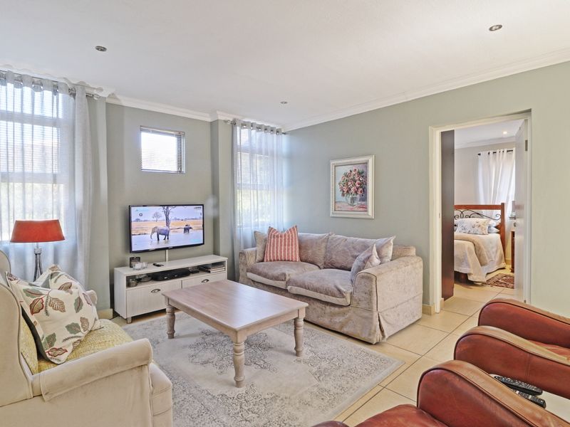 A comfortable living room featuring tiled flooring, recessed downlighting, and neutral wall tones, with an adjacent bedroom visible through the doorway.