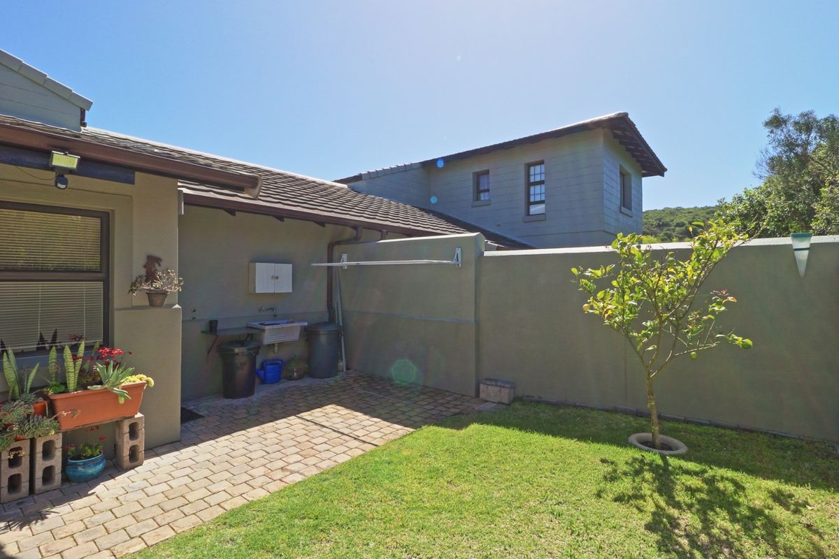 A private rear courtyard featuring a paved patio area, utility sink, wall-mounted drying rack, and a small lawn with a boundary wall.