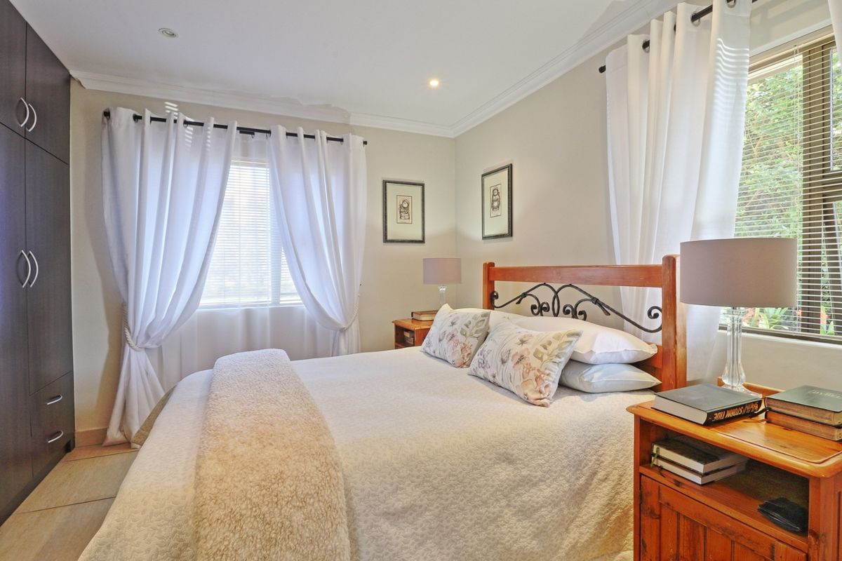 A well-maintained bedroom featuring built-in cupboards, recessed downlighting, and large windows with venetian blinds, offering a bright and comfortable living space.
