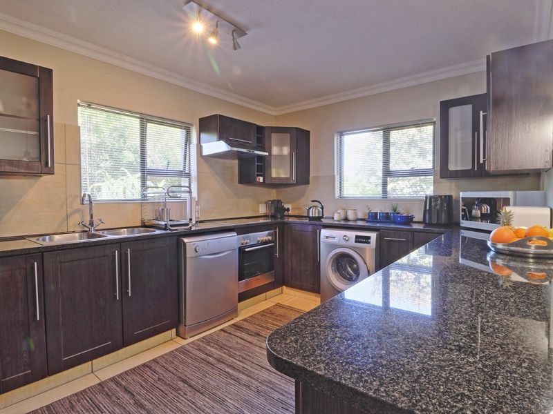 A well-maintained kitchen featuring dark wood cabinetry, granite countertops, a built-in oven, extractor fan, and integrated dishwasher with ample workspace.