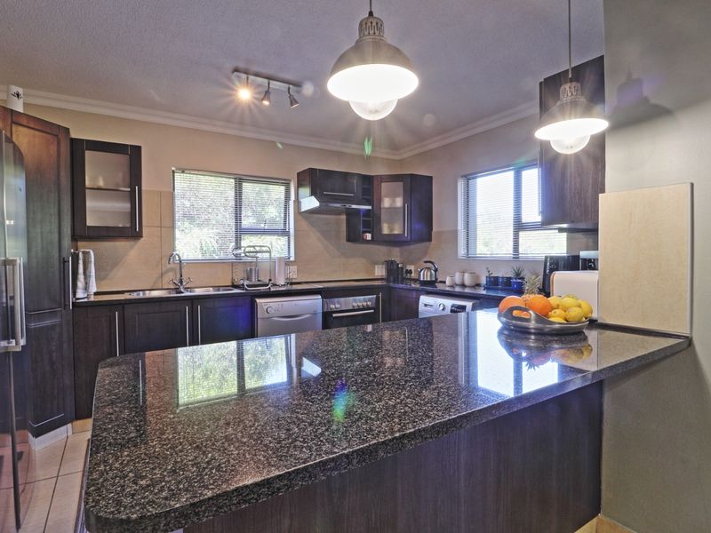 Modern kitchen featuring dark wood cabinetry, granite countertops, stainless steel appliances, and stylish pendant lighting, offering a functional and well-maintained cooking space.