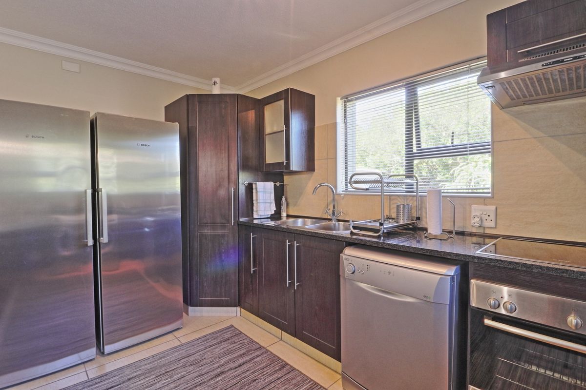 A functional kitchen featuring dark wood cabinetry, granite countertops, integrated oven, extractor fan, and a stainless steel sink with a window view.