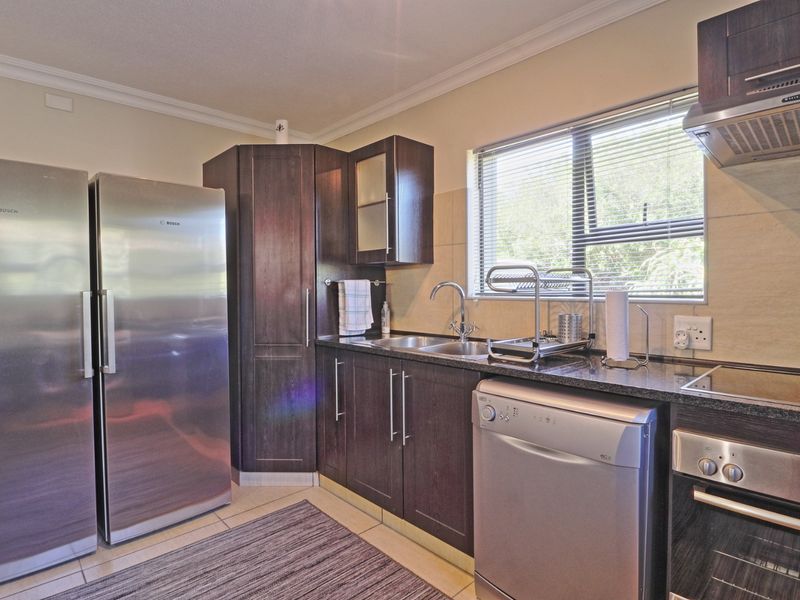 A functional kitchen featuring dark wood cabinetry, granite countertops, integrated oven, extractor fan, and a stainless steel sink with a window view.