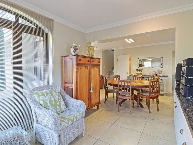 Open-plan living and dining area featuring tiled flooring, coved cornicing, and a large arched window with venetian blinds.