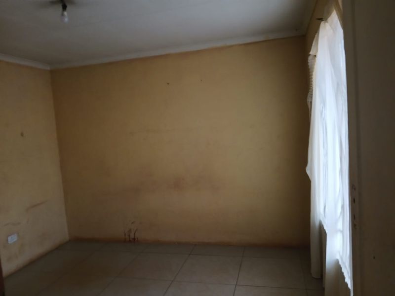 An empty bedroom featuring tiled flooring and coved ceilings, currently requiring cosmetic updates to the wall finishes.