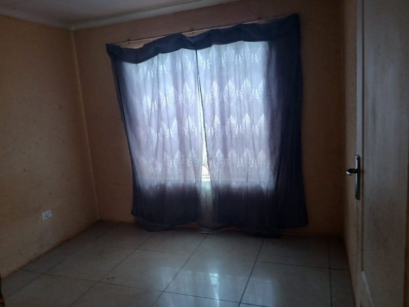 An empty bedroom featuring tiled flooring and a window with curtains, requiring cosmetic updates to the wall finishes.