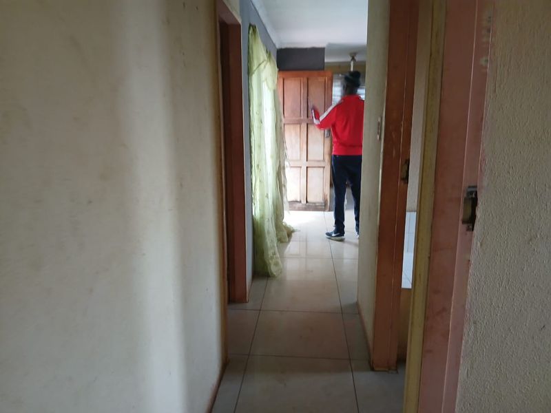 A narrow interior hallway featuring tiled flooring and wooden door frames, showing significant signs of wear and requiring cosmetic updates.