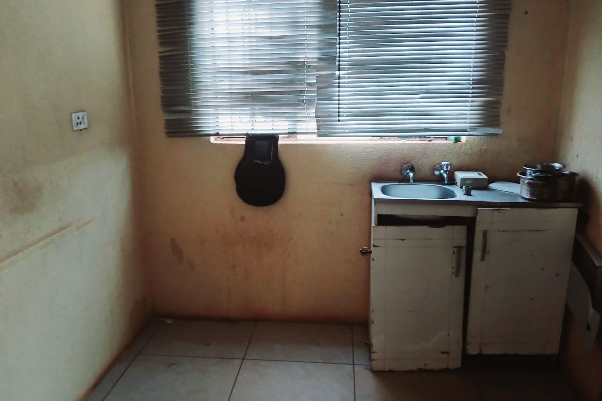 A small, dated kitchen area featuring a basic stainless steel sink, base cabinetry, and tiled flooring, requiring significant cosmetic updates and repairs.