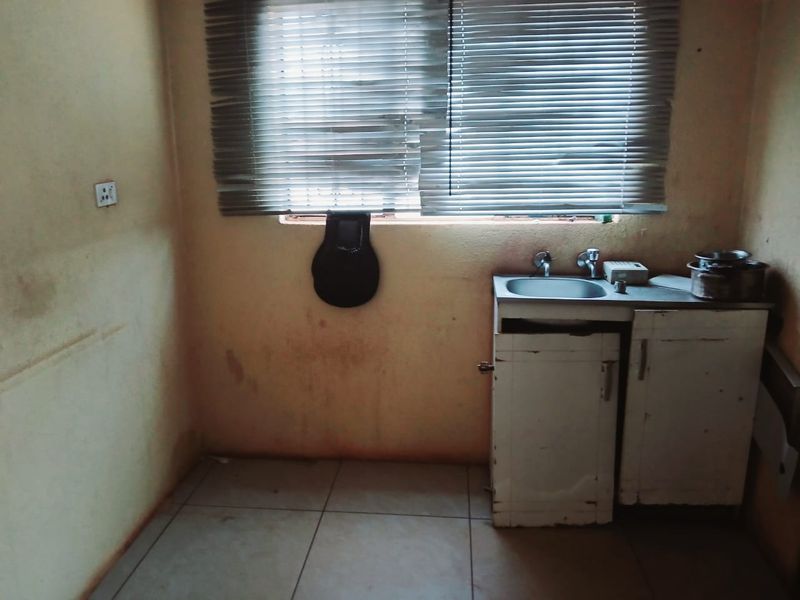 A small, dated kitchen area featuring a basic stainless steel sink, base cabinetry, and tiled flooring, requiring significant cosmetic updates and repairs.